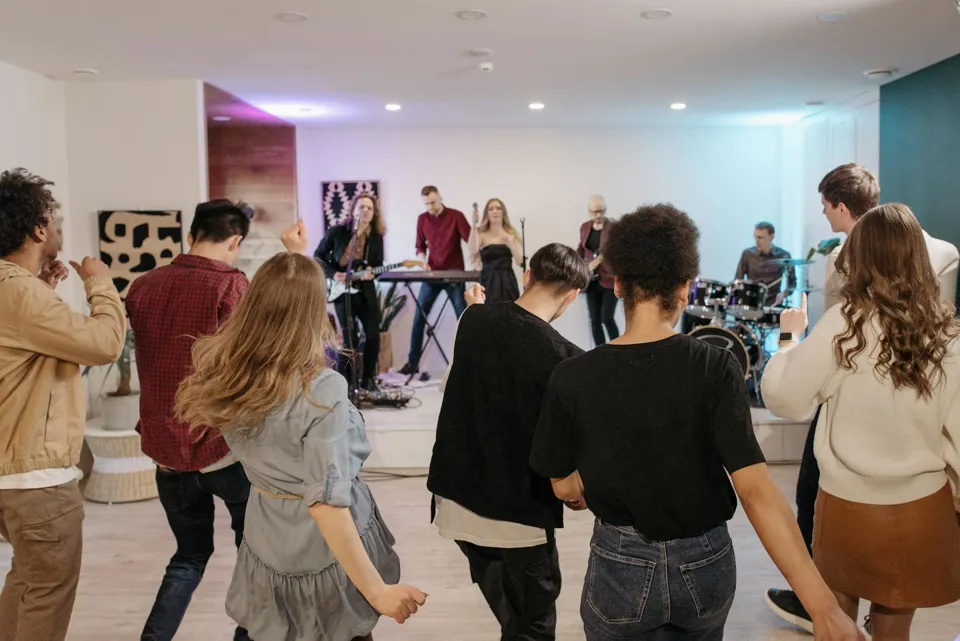 Eine Gruppe von Menschen in einem Raum, in dem eine Band auf der Bühne spielt.