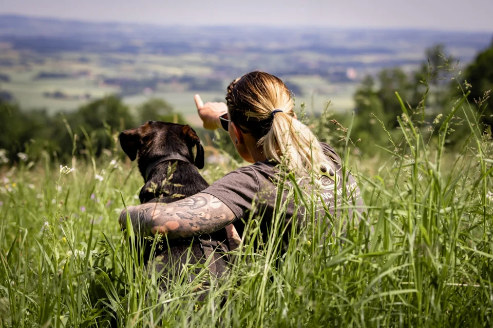 Hundecoach sitzt mit ihrem Hund Balu im hohen Gras