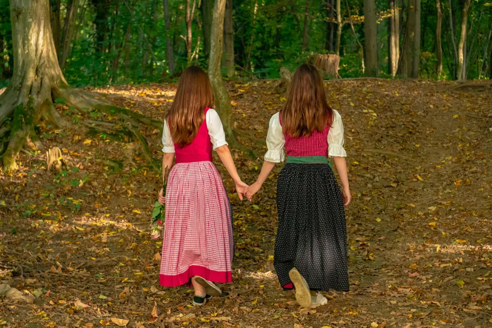 Zwei Frauen, die Händchen haltend durch den Wald gehen.