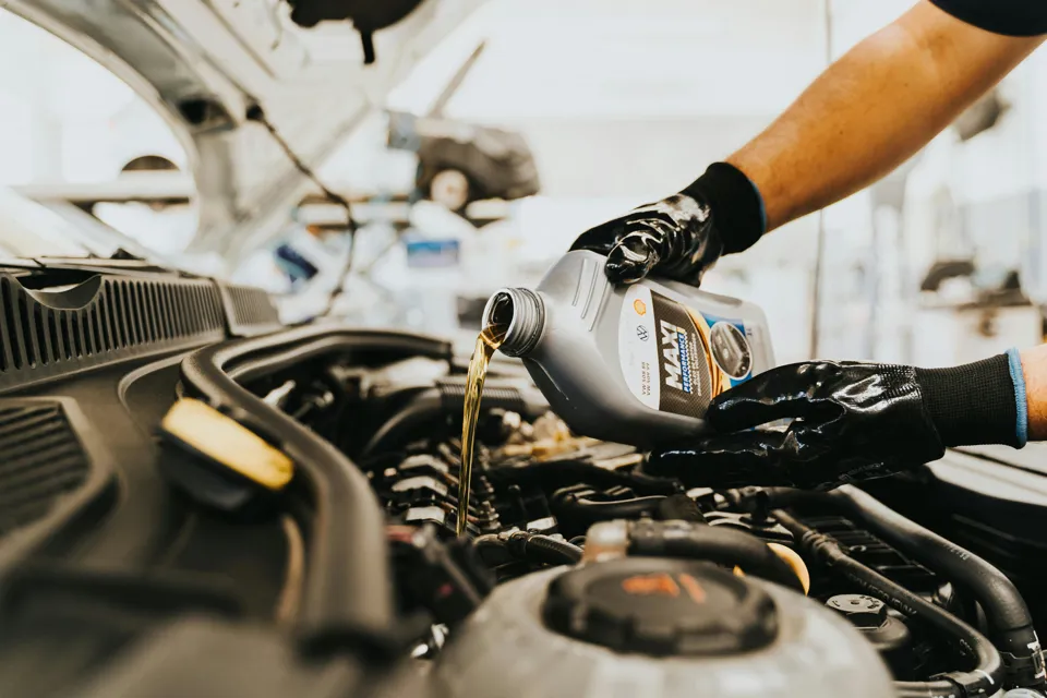 Eine Person gießt Öl in einen Automotor.