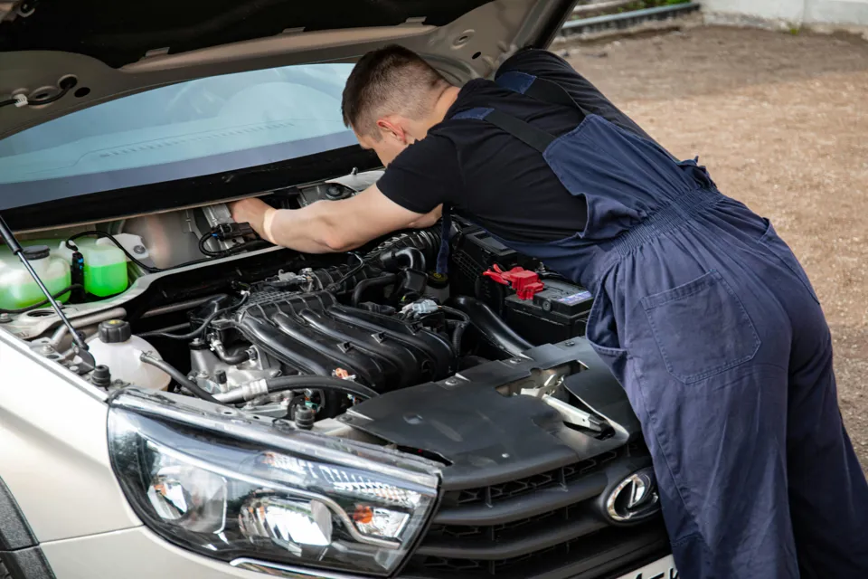Eine Person in Overalls arbeitet unter der Motorhaube eines Autos.