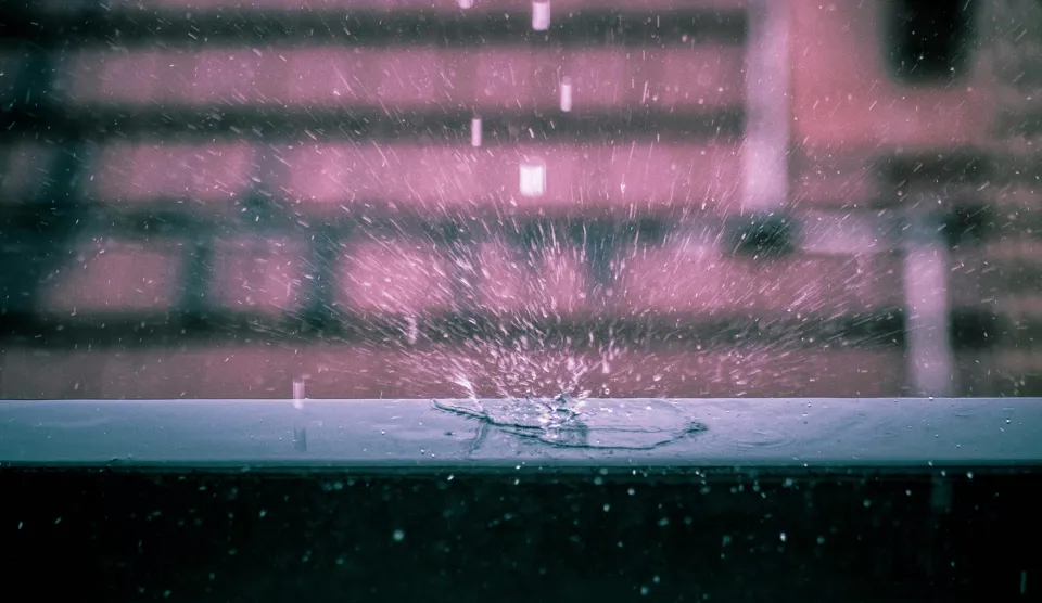 Wassertropfen, die auf eine Fensterbank fallen.