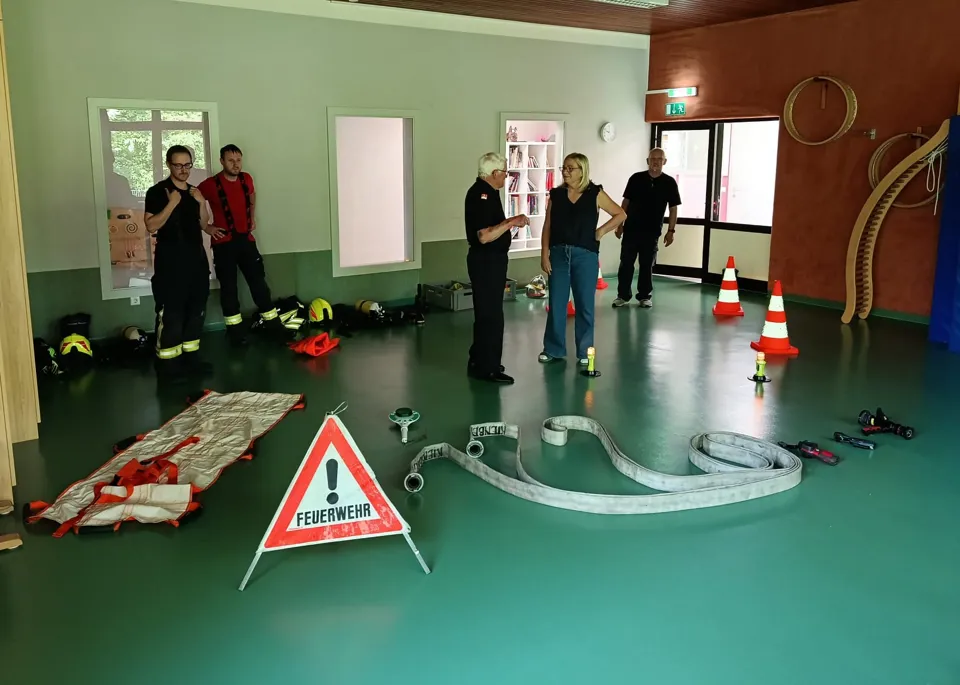 Eine Gruppe von Personen steht in einem Raum mit einem Feuerwehrschlauch und Sicherheitsausrüstung.