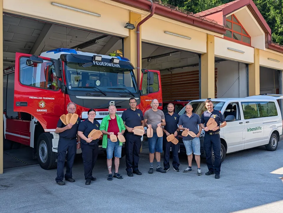 Eine Gruppe von Menschen hält hölzerne Gegenstände vor einem Feuerwehrauto.