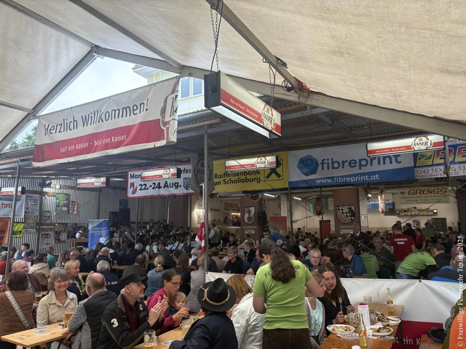 Eine große Gruppe von Menschen sitzt an Tischen in einem Zelt.