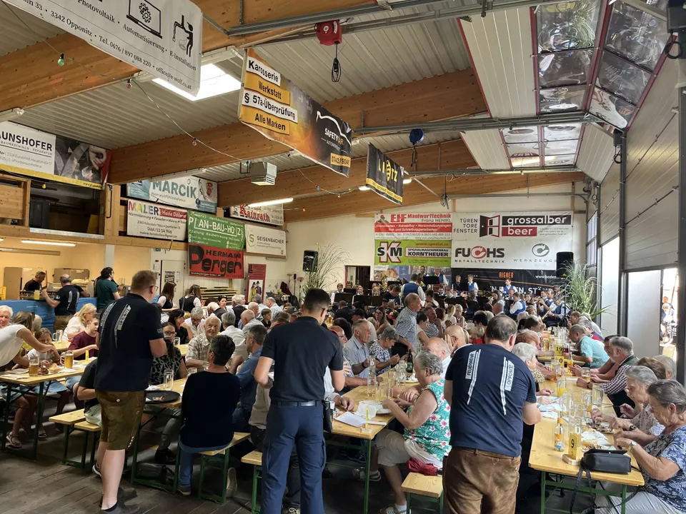 Eine große Gruppe von Menschen sitzt an Tischen in einem Raum.