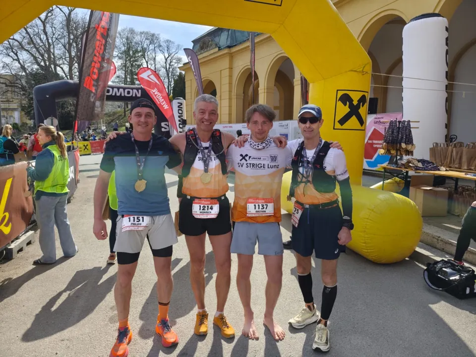 Eine Gruppe von Männern, die Medaillen tragen und vor einem aufblasbaren Bogen stehen.