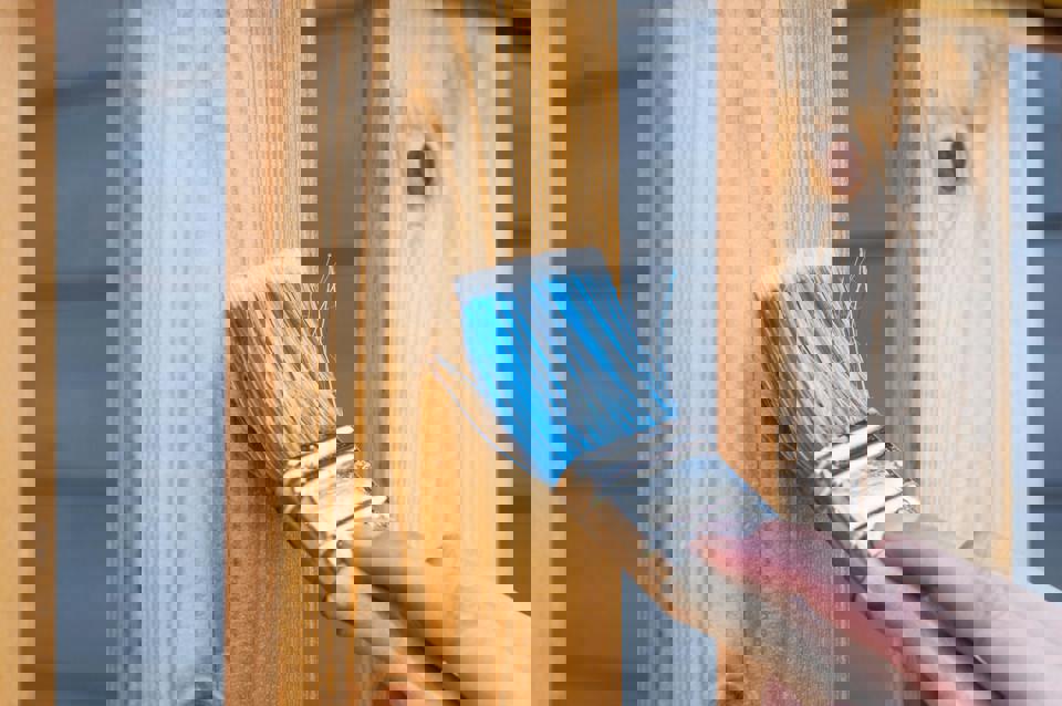 Eine Hand hält einen Pinsel über einem Holzzaun.