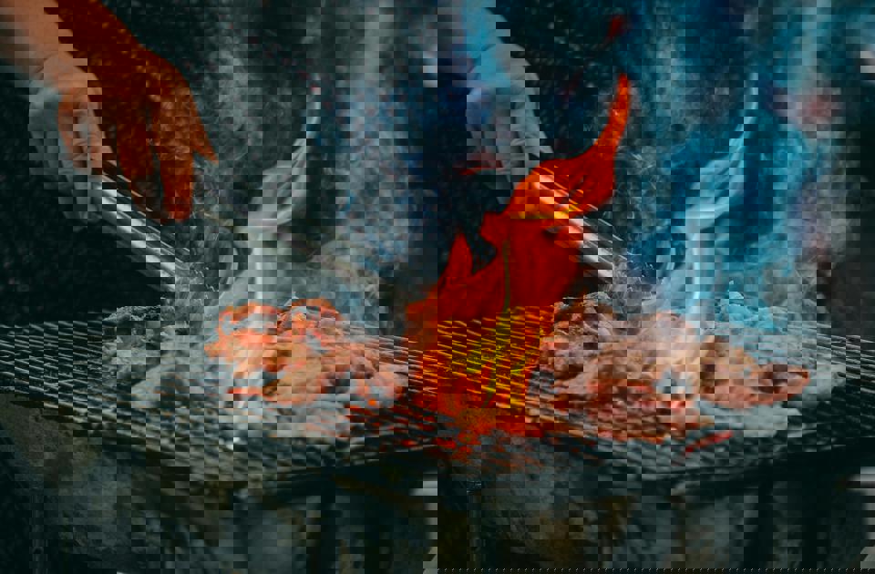 Eine Person hält eine Zange über Essen auf einem Grill.