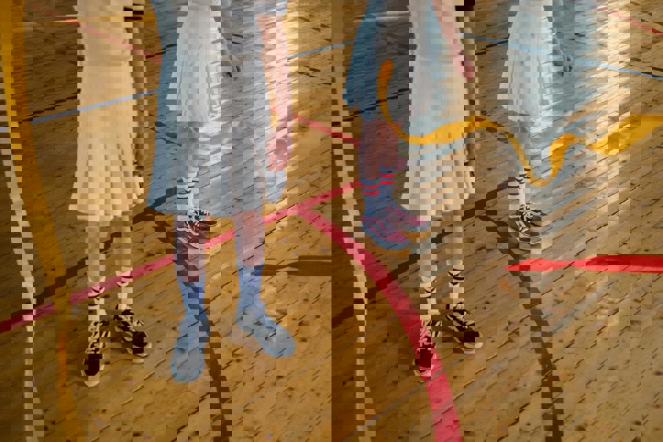 Zwei Kinder in weißen Röcken und roten Socken auf einem Holzboden.