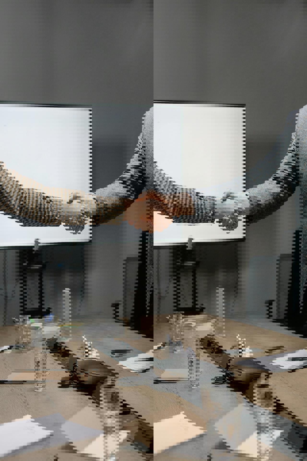 Eine Person schüttelt einer anderen Person vor einem weißen Bildschirm die Hand.