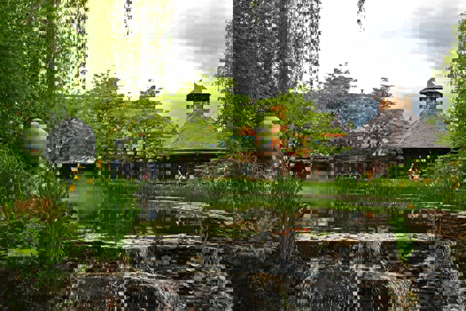 Ein Teich mit einem Wasserfall und einer Statue einer Person im Hintergrund.