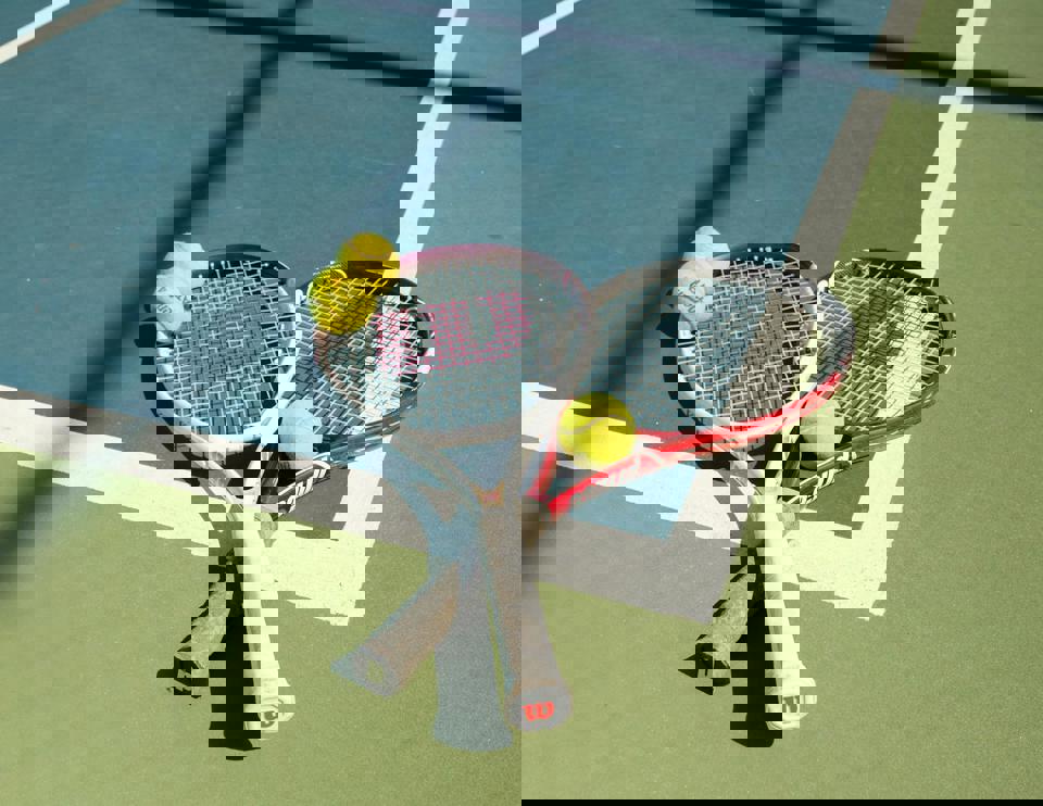 Zwei Tennisschläger und Bälle auf einem Tennisplatz.