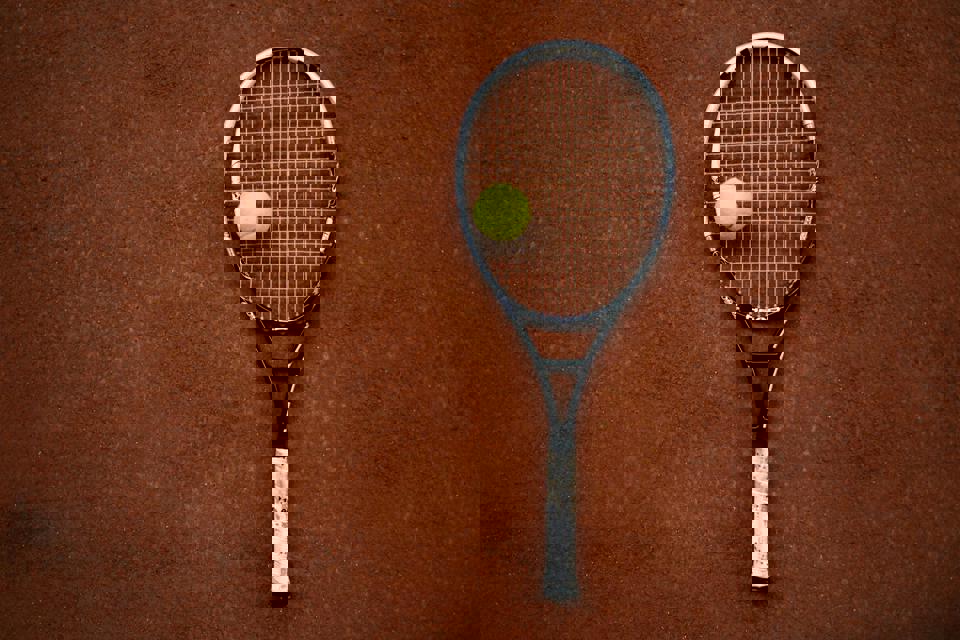 Ein Tennisschläger und ein Ball auf einem Sandplatz.